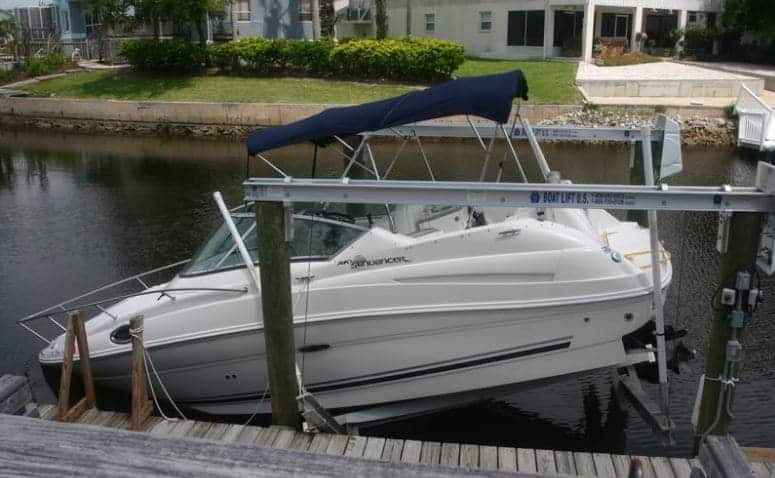 White boat with navy covering is held above the water for Boat Lift Maintenance