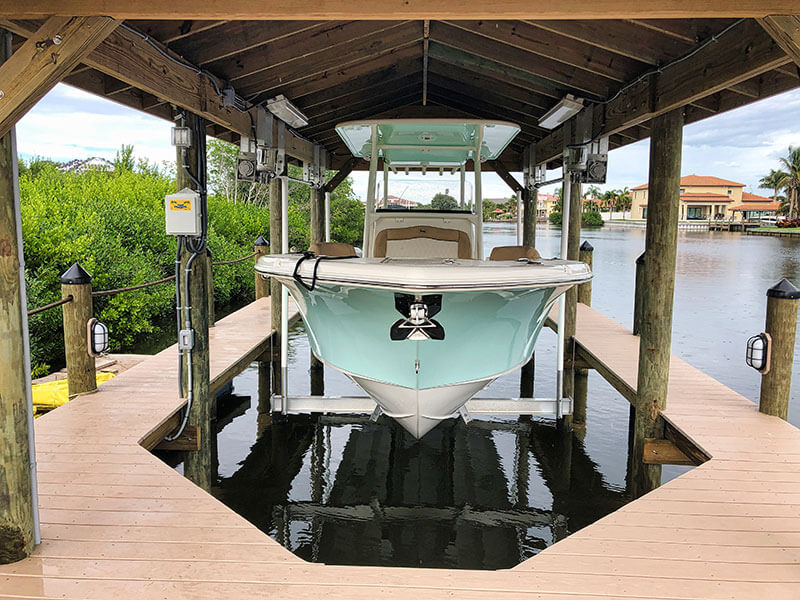Mint green and white boat hangs above the water in an IMM Quality boathouse lift
