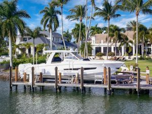 boat lift with stepped top beam holds large white boat in front of waterfront home